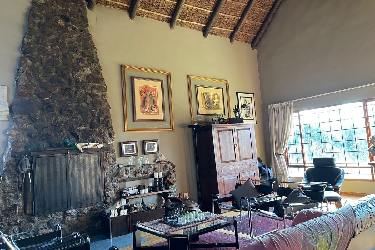 Spacious living room featuring a prominent stone fireplace, high vaulted ceilings with exposed timber rafters, and a thatched roof finish.