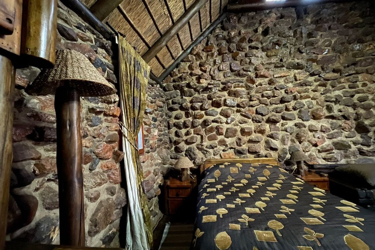 A rustic bedroom featuring distinctive exposed stone walls, a traditional thatched roof, and exposed timber rafters, creating a unique farm-style atmosphere.