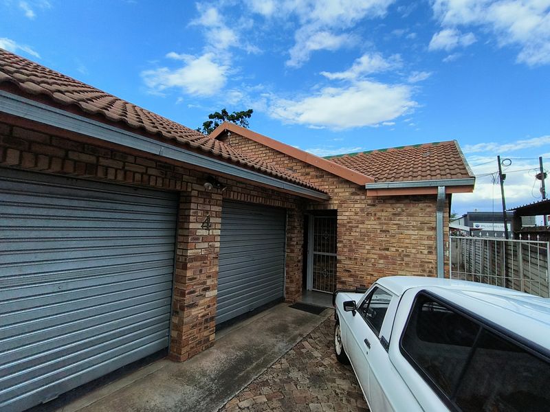 Front elevation of a face brick house featuring a double garage with roller shutter doors and a paved driveway.
