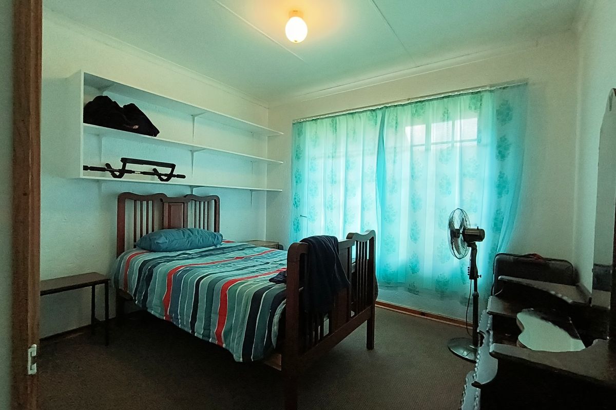 A functional bedroom featuring built-in wall shelving, carpeted flooring, and a large window with natural light.