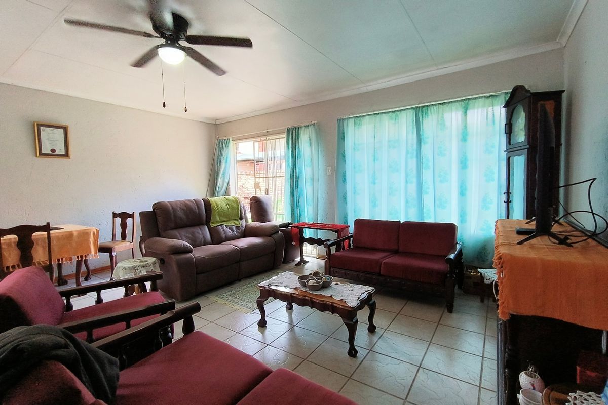 A spacious living room featuring tiled flooring, a ceiling fan, and large windows with natural light, providing a comfortable and functional living space.