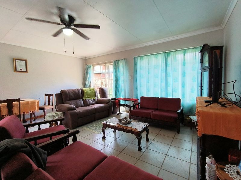 A spacious living room featuring tiled flooring, a ceiling fan, and large windows with natural light, providing a comfortable and functional living space.