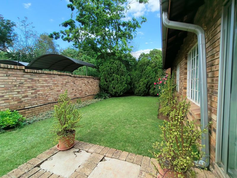 A private rear garden featuring a brick boundary wall, a small paved patio area, and a well-maintained lawn with established greenery.