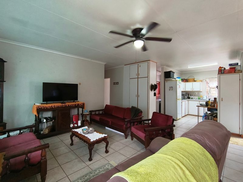 Open-plan living area featuring tiled flooring, a ceiling fan, and an adjoining kitchen with built-in cabinetry.