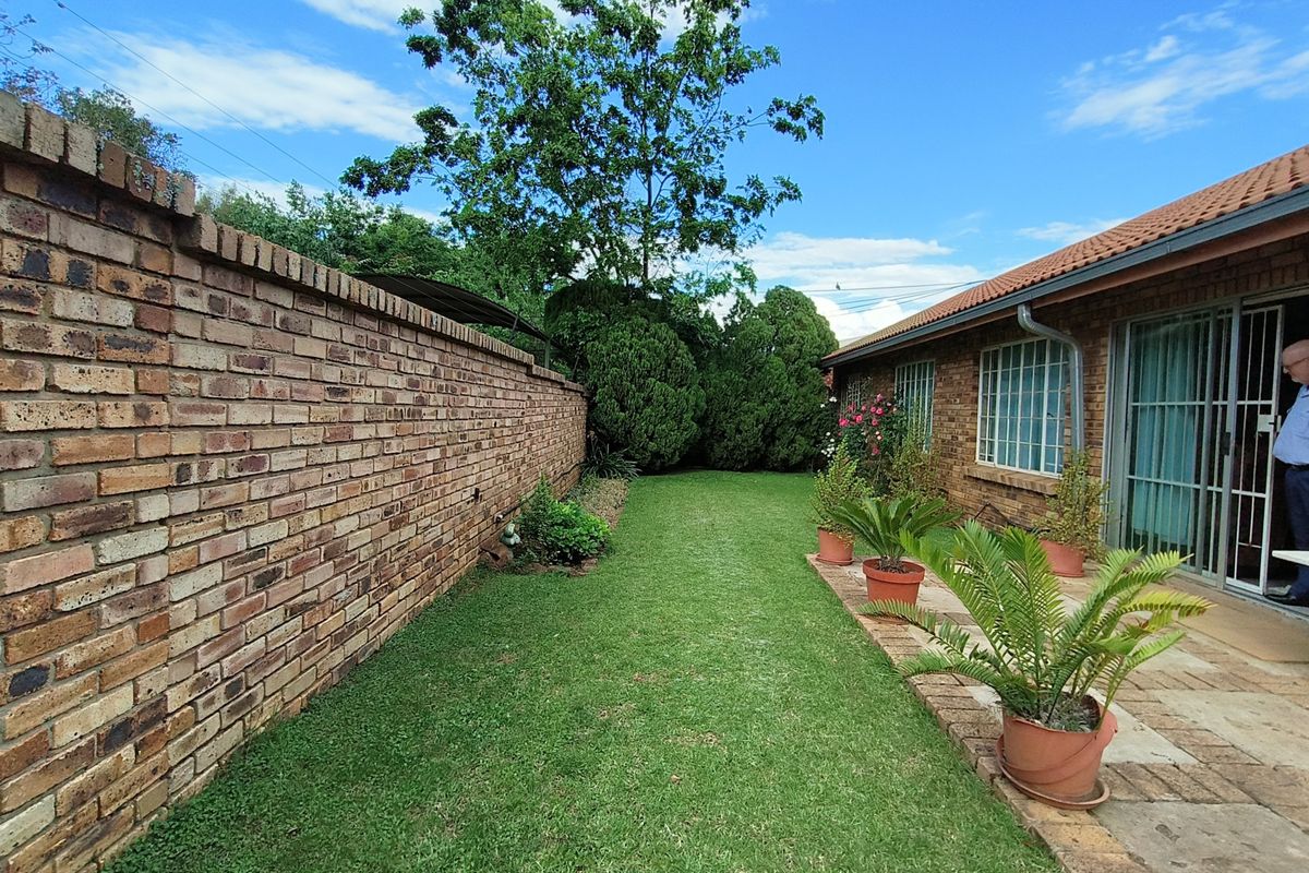 A well-maintained rear garden featuring a brick boundary wall, a paved walkway, and a neat lawn area adjacent to the house.