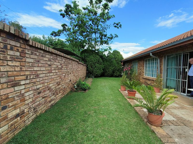 A well-maintained rear garden featuring a brick boundary wall, a paved walkway, and a neat lawn area adjacent to the house.