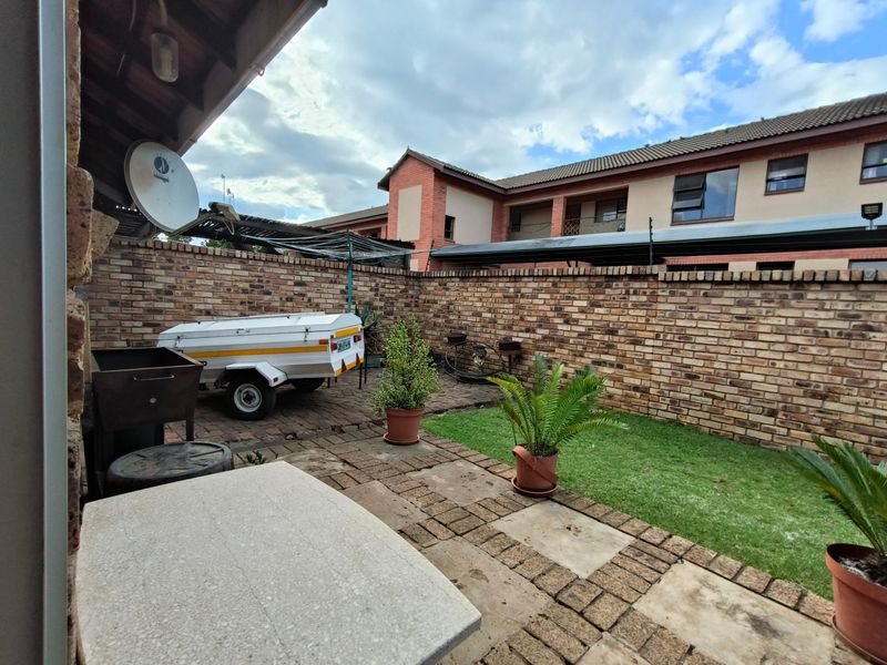 A private rear courtyard featuring a paved patio area, a small lawn, and a high brick boundary wall for added privacy.