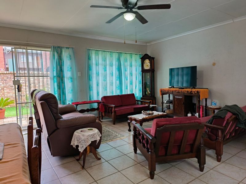 A living room featuring tiled flooring, a ceiling fan, and a sliding glass door providing access to the exterior.