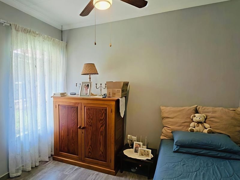 A functional bedroom featuring laminate flooring, a ceiling fan, and a built-in cupboard, offering a neutral canvas for personalization.