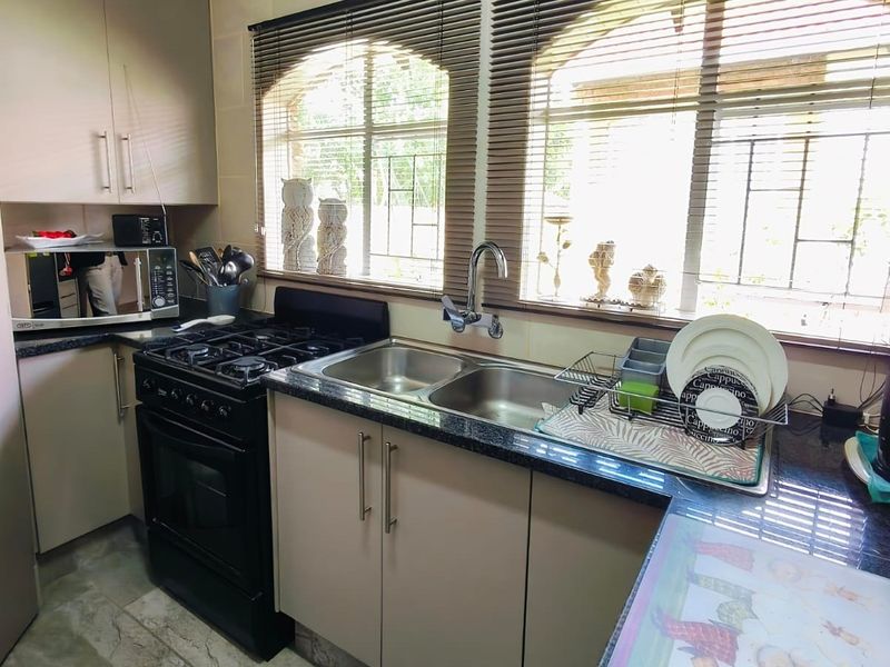 A functional kitchen featuring built-in cabinetry, granite countertops, a double basin sink, and a gas stove with oven.
