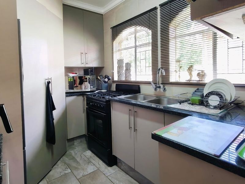 A functional kitchen featuring built-in cabinetry, granite countertops, a double basin sink, and a freestanding oven, complemented by tiled flooring and natural light.