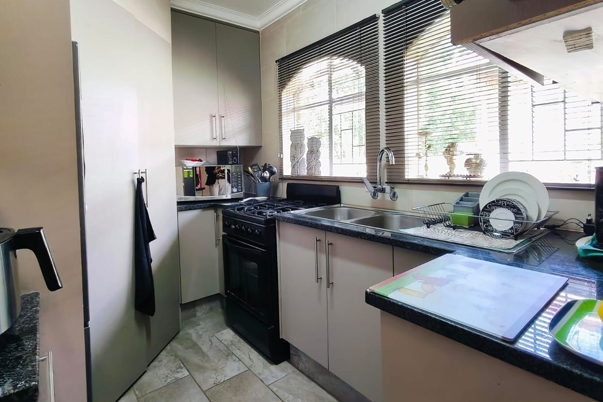 A functional kitchen featuring built-in cabinetry, granite countertops, a double basin sink, and a freestanding oven, complemented by tiled flooring and natural light.