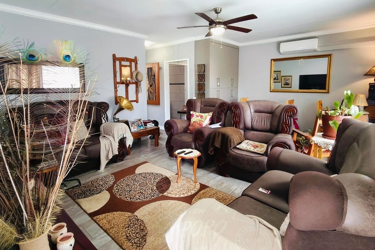 A comfortable living room featuring laminate flooring, a ceiling fan, and a wall-mounted split-system air conditioner, with built-in storage cupboards.