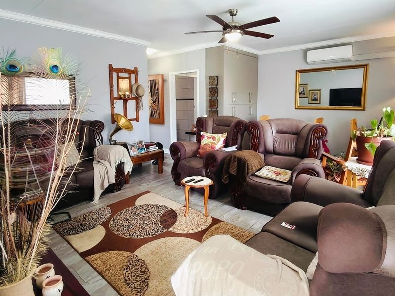 A comfortable living room featuring laminate flooring, a ceiling fan, and a wall-mounted split-system air conditioner, with built-in storage cupboards.