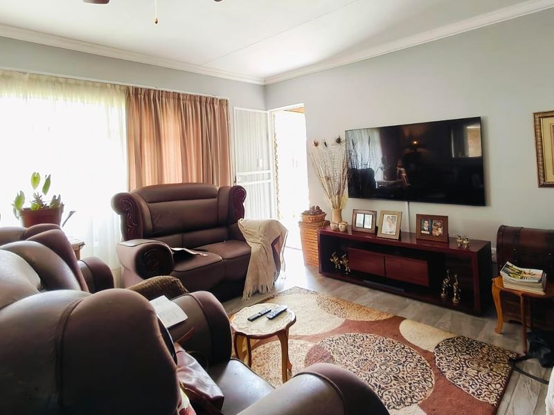 A comfortable living room featuring laminate flooring, cove cornicing, and direct access to an outdoor area through a security gate.