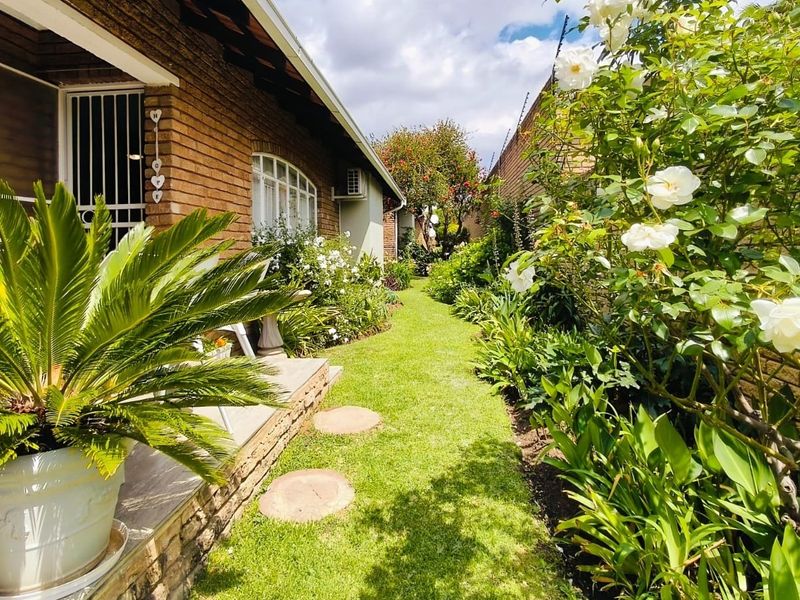 A well-maintained rear garden featuring a brick facade, paved walkway, and established landscaping with rose bushes and greenery.