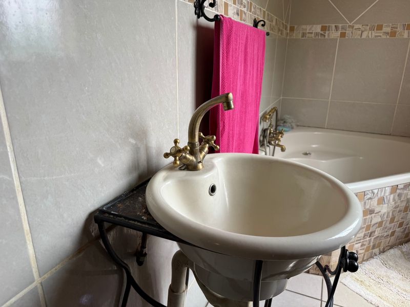 A bathroom featuring a pedestal basin with brass fixtures, a built-in bathtub, and decorative mosaic tile accents on the walls.