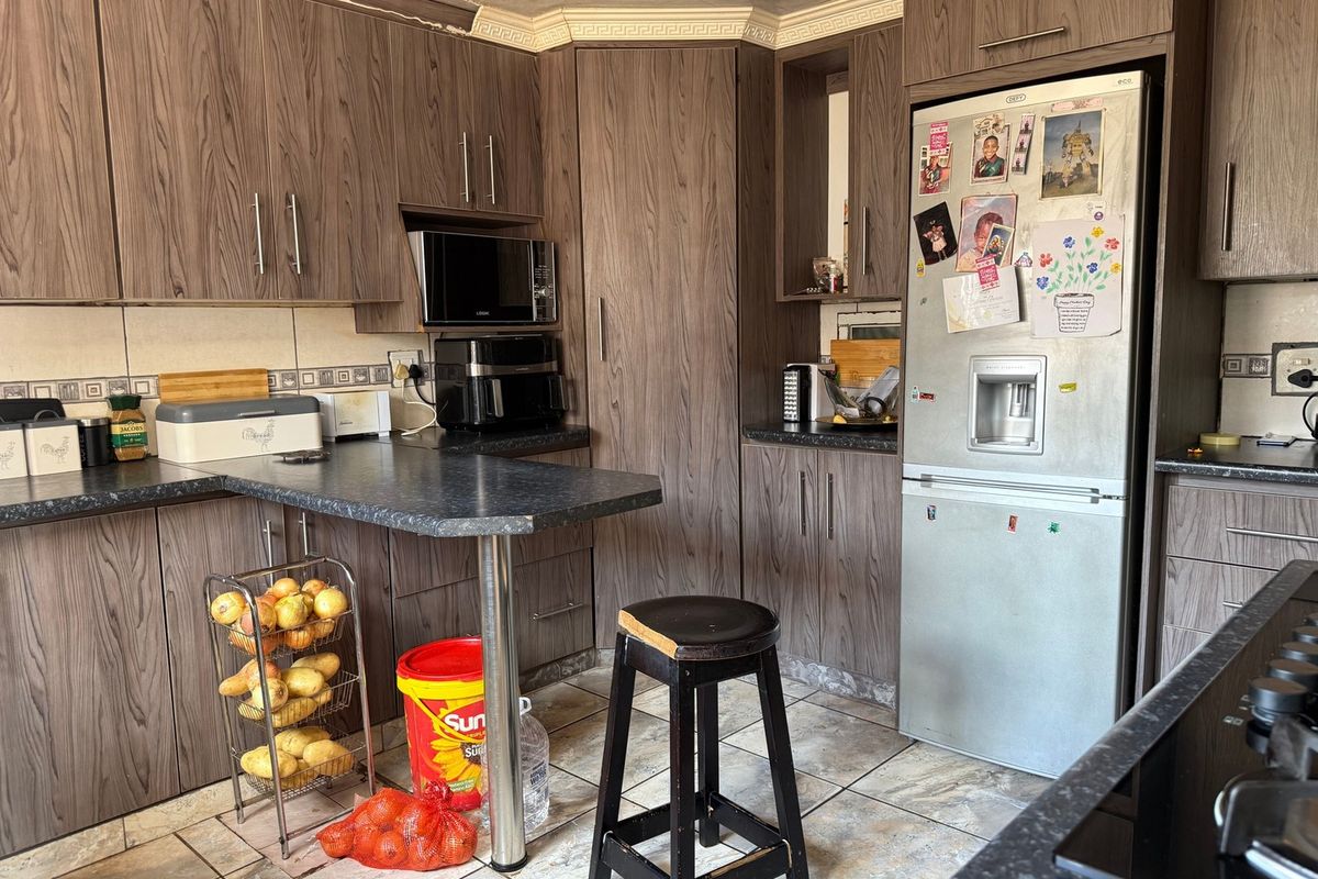 A functional kitchen featuring wood-look laminate cabinetry, dark countertops, and tiled flooring, offering a practical layout with integrated appliance space.