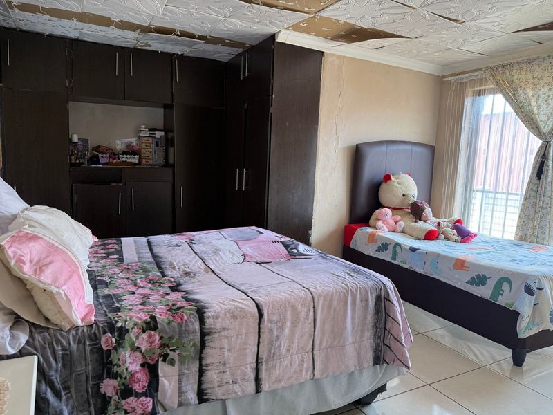 A bedroom featuring built-in cupboards and tiled flooring, currently showing signs of wear including damaged ceiling tiles and cracked wall plaster.