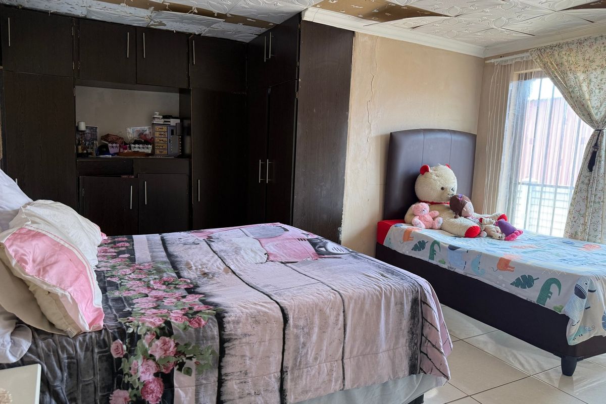 A bedroom featuring built-in cupboards and tiled flooring, currently showing signs of wear including damaged ceiling tiles and cracked wall plaster.