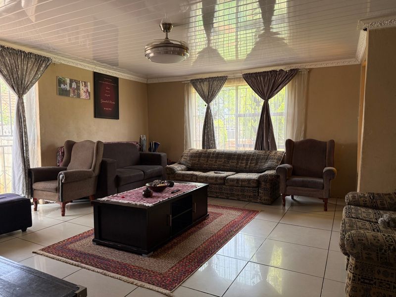 A spacious living room featuring tiled flooring, a ceiling fan, and large windows with security bars, offering a functional and comfortable living space.