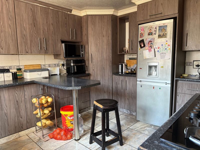 A functional kitchen featuring wood-look laminate cabinetry, dark countertops, and tiled flooring, offering a practical layout with integrated appliance space.