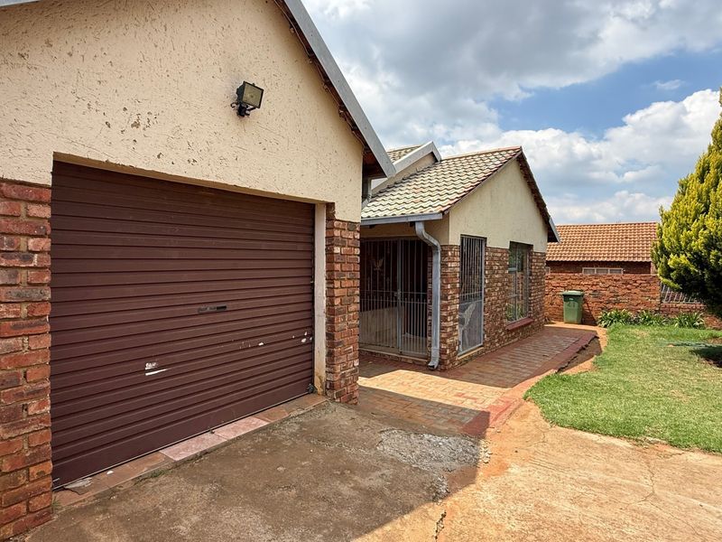 Front view of the property featuring a single roller garage, brick exterior walls, tiled roof, and a paved entrance walkway with security gates.