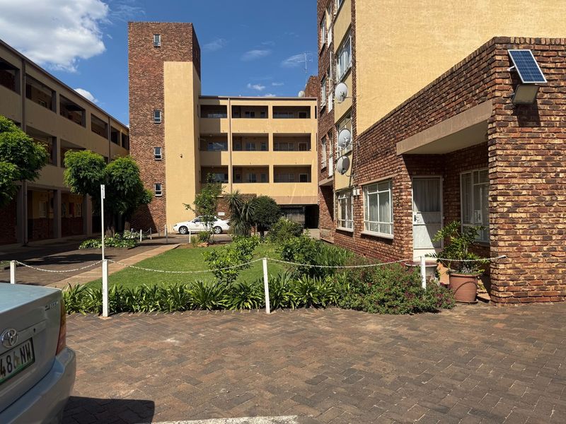Exterior view of an apartment complex featuring brick facades, a central landscaped garden area, and paved driveway access.