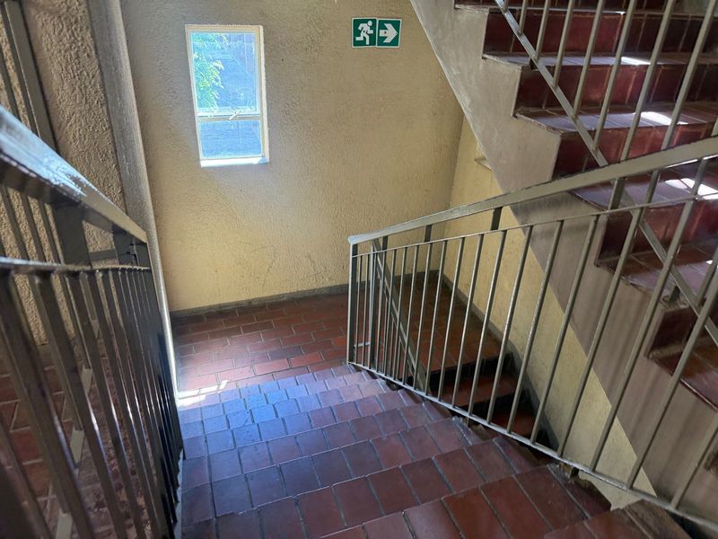 A functional apartment stairwell featuring tiled steps, metal handrails, and a small window providing natural light.