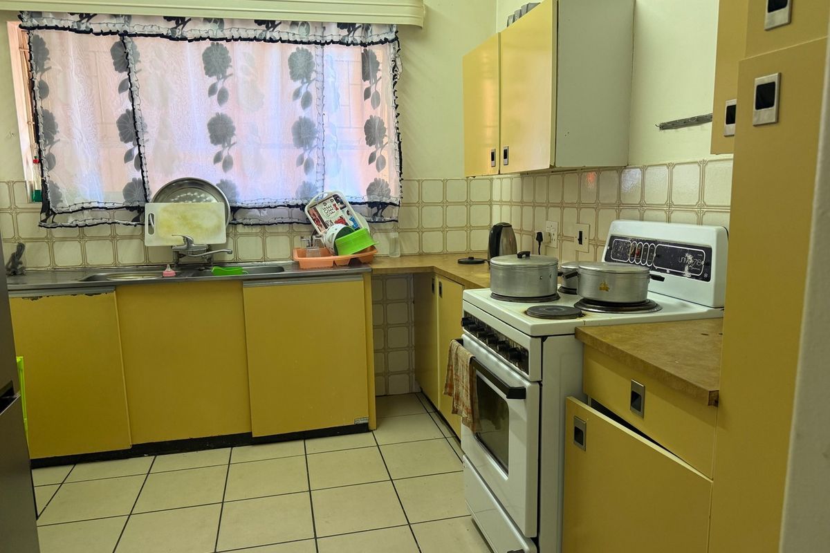 A dated kitchen featuring original yellow cabinetry, tiled backsplash, and ceramic flooring, offering significant potential for a modern renovation.