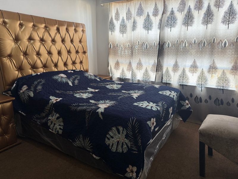 A bedroom featuring carpeted flooring and a large window with patterned curtains.
