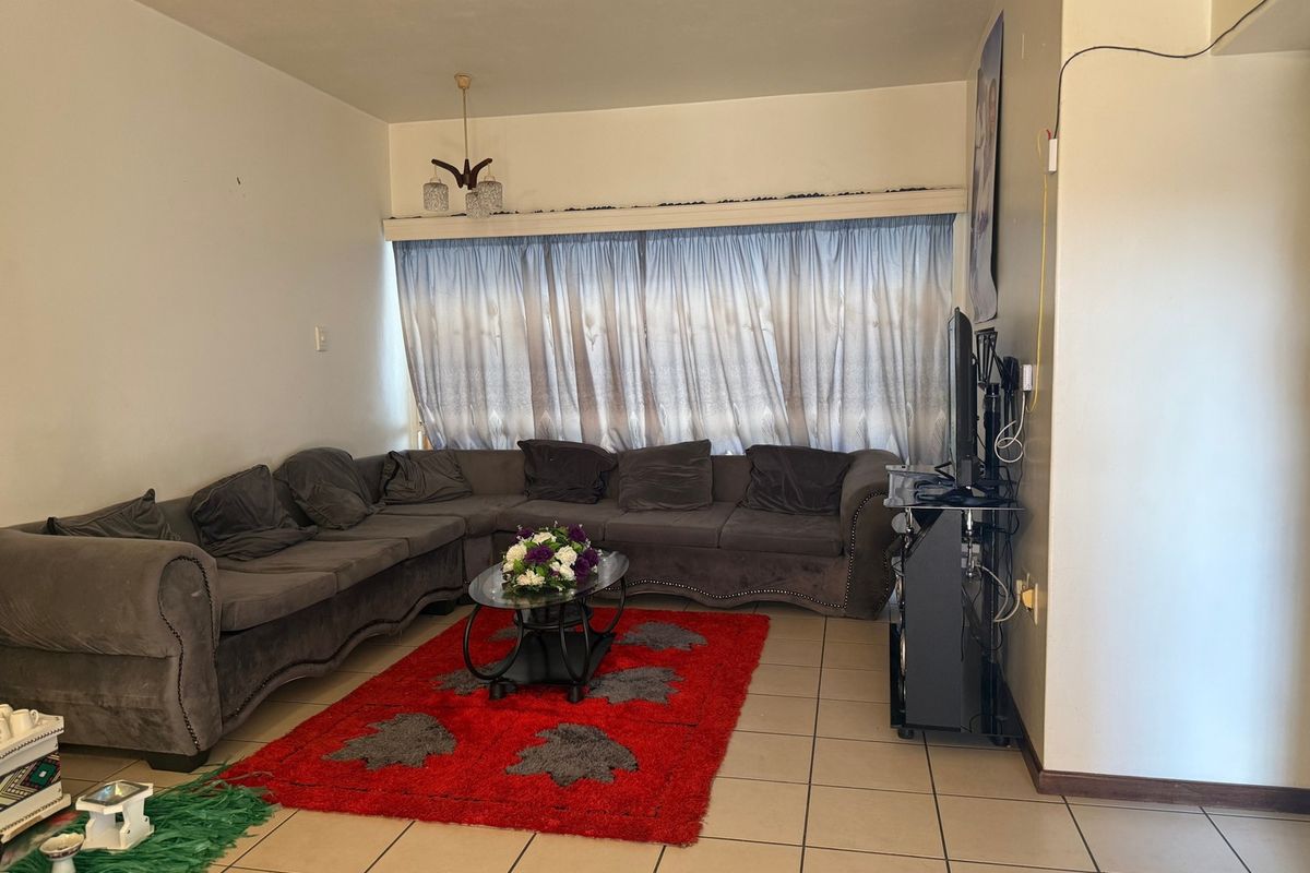 A living room featuring tiled flooring and a large window with curtain rails, providing a functional space for relaxation.