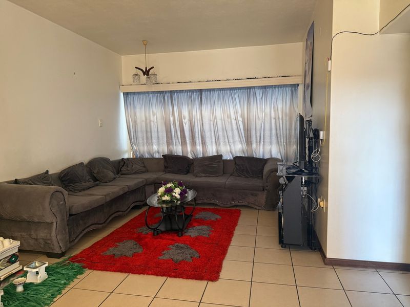 A living room featuring tiled flooring and a large window with curtain rails, providing a functional space for relaxation.
