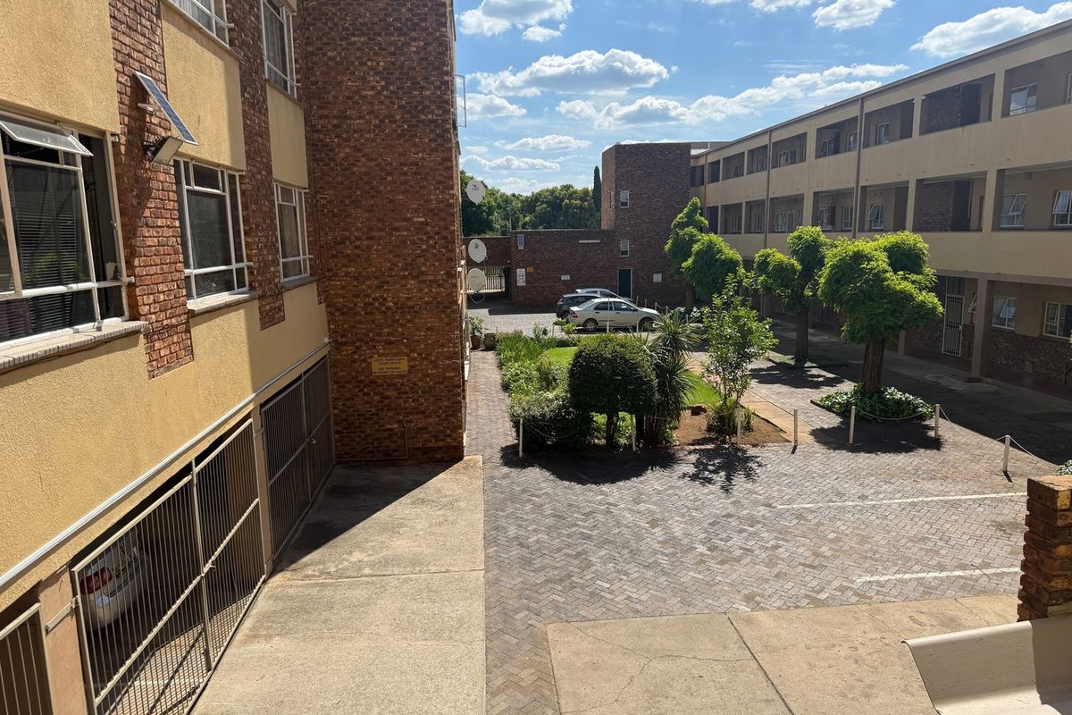 An elevated view of the apartment complex courtyard featuring paved parking areas, landscaped garden beds, and brick building facades.