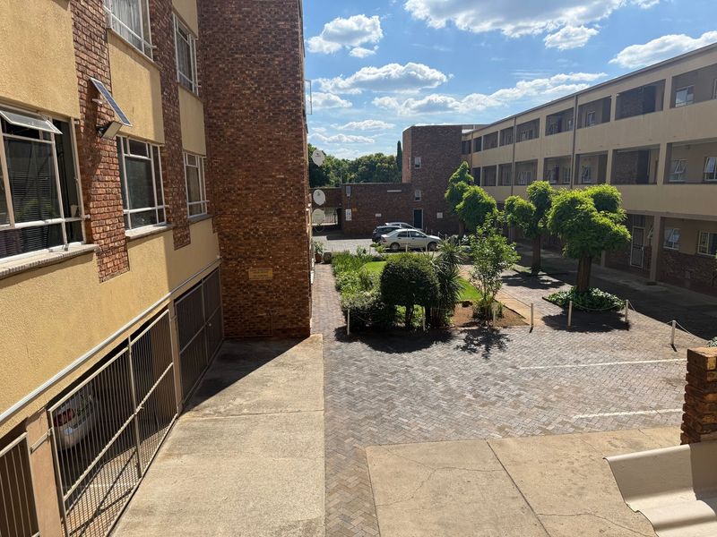 An elevated view of the apartment complex courtyard featuring paved parking areas, landscaped garden beds, and brick building facades.