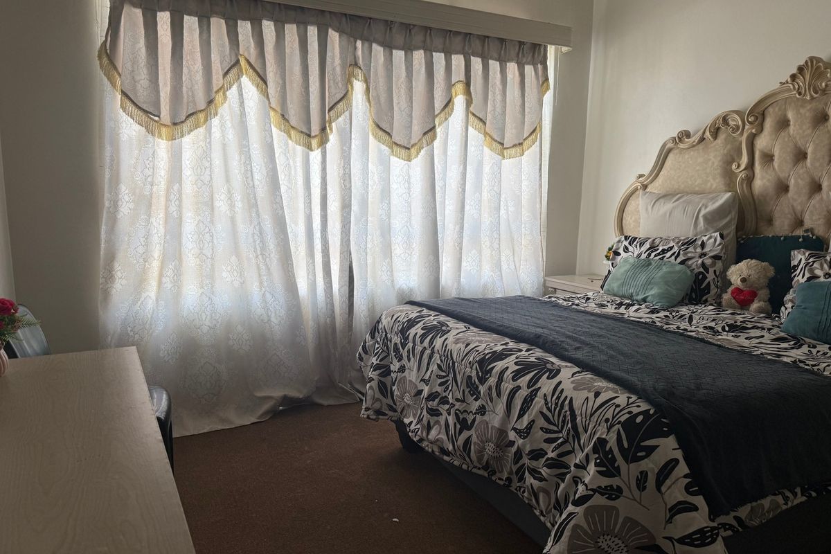 A bedroom featuring carpeted flooring and a large window with decorative curtains.