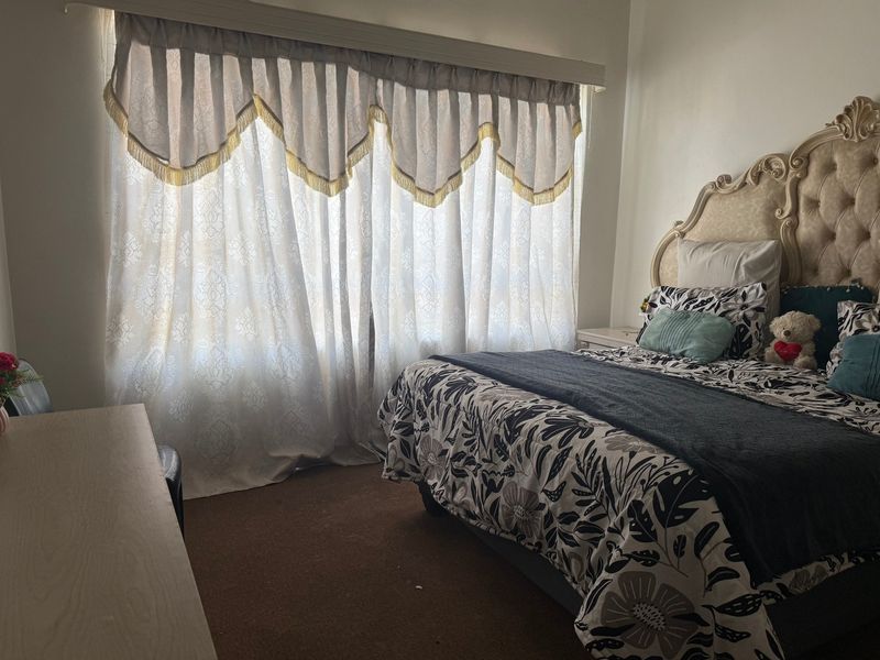 A bedroom featuring carpeted flooring and a large window with decorative curtains.