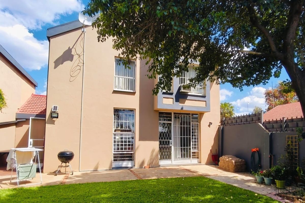Rear view of the townhouse featuring a paved patio area, established garden, and secure window and door fittings.