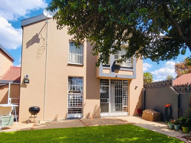 Rear view of the townhouse featuring a paved patio area, established garden, and secure window and door fittings.