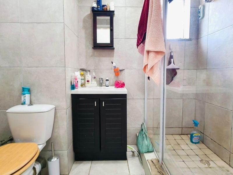 A functional bathroom featuring a vanity cabinet, toilet, and a glass-enclosed shower with tiled finishes throughout.