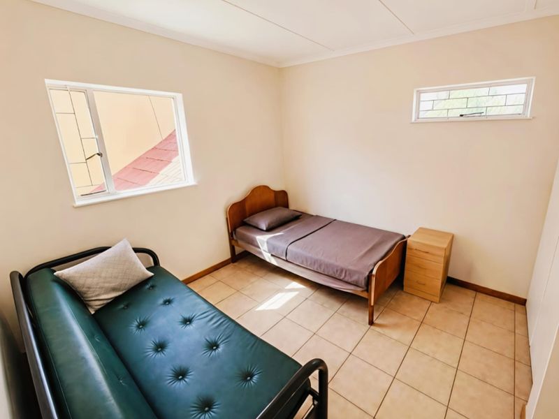 A simple bedroom featuring tiled flooring and dual windows providing natural light.