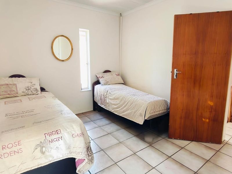A functional bedroom featuring tiled flooring, a wooden door, and a vertical window, providing a simple and practical living space.
