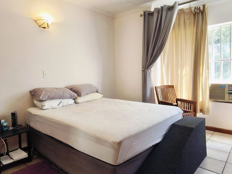 A bedroom featuring tiled flooring, a window-mounted air conditioning unit, and a wall-mounted light fixture.