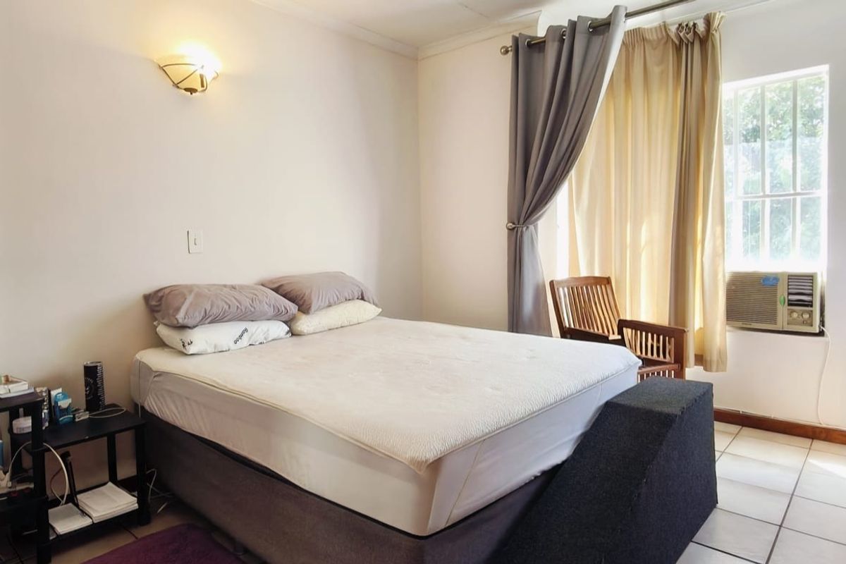 A bedroom featuring tiled flooring, a window-mounted air conditioning unit, and a wall-mounted light fixture.