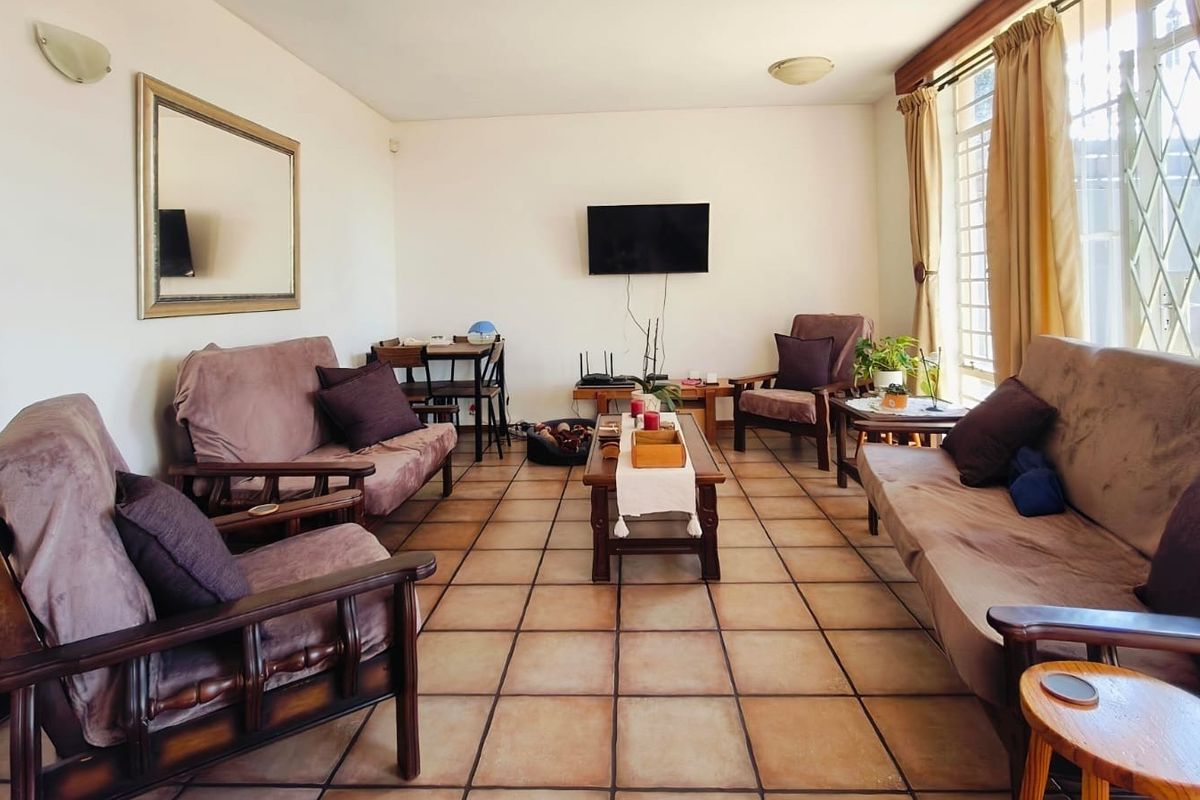 A spacious living room featuring traditional terracotta-style floor tiles and large windows with security gates, offering a functional and well-lit living area.