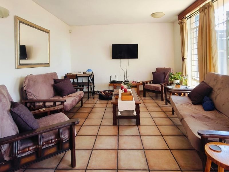 A spacious living room featuring traditional terracotta-style floor tiles and large windows with security gates, offering a functional and well-lit living area.