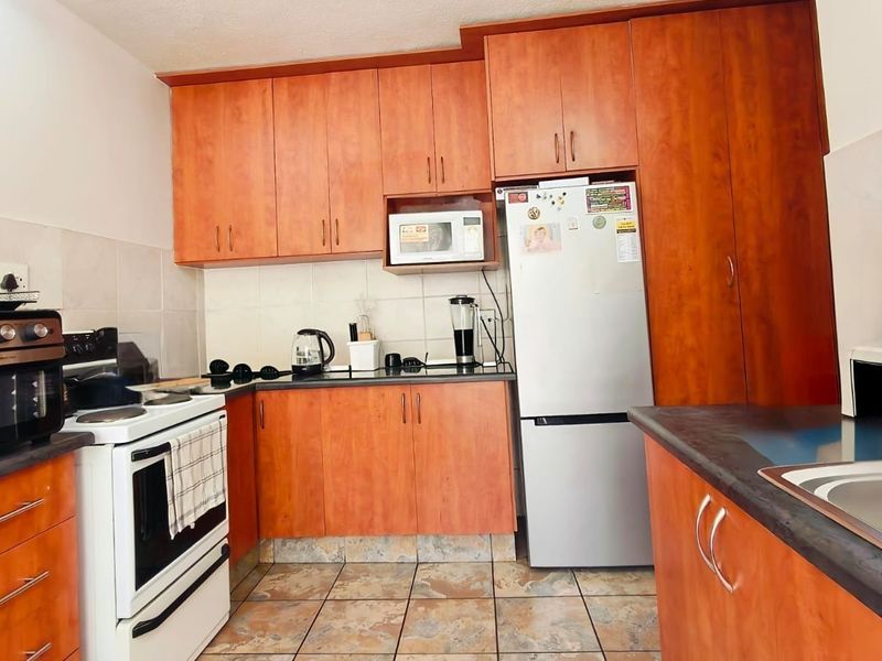 A functional kitchen featuring wood-look laminate cabinetry, dark countertops, tiled backsplash, and ceramic floor tiles with a built-in oven and hob.