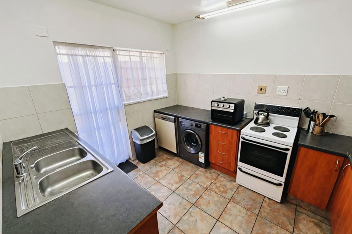 Functional kitchen featuring tiled flooring, laminate countertops, double basin sink, and built-in cabinetry with space for appliances.
