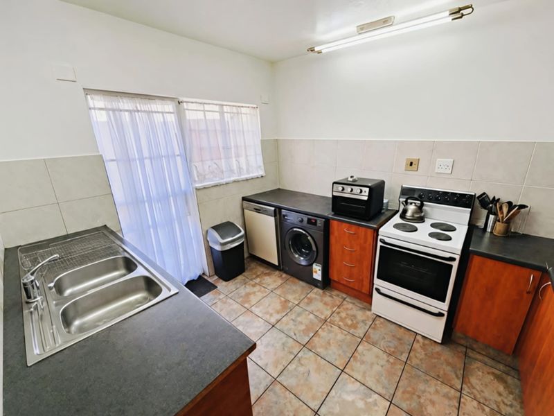Functional kitchen featuring tiled flooring, laminate countertops, double basin sink, and built-in cabinetry with space for appliances.