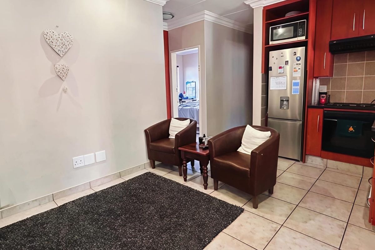 Open-plan living area featuring a compact kitchen with built-in cabinetry, integrated appliances, and tiled flooring throughout.